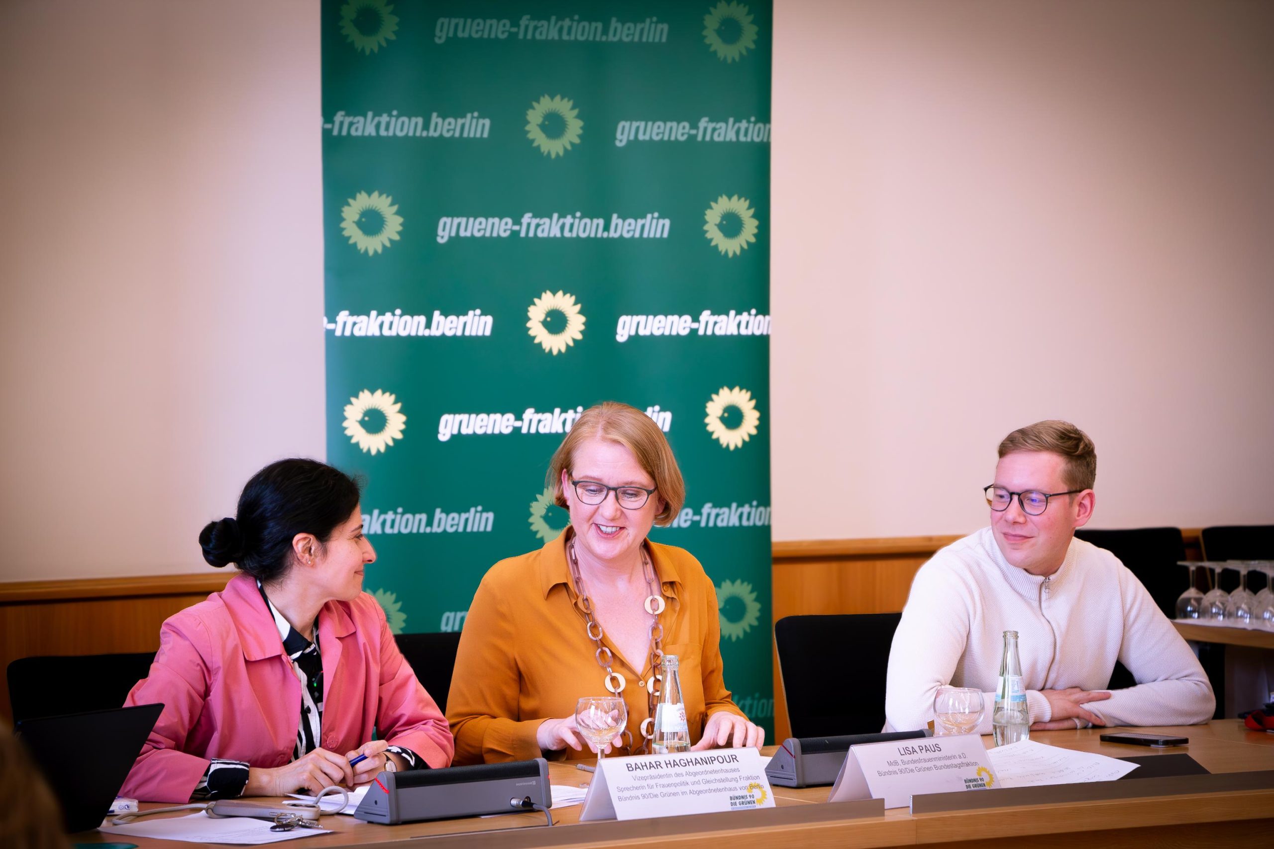 Auf dem Foto sieht man von links nach rechts: Bahar Haghanipour, Lisa Paus und Vasili Franco. Sie sitzen an einem Tisch. Vor ihnen Namensschilder, hinter ihnen Banner der Grünen Fraktion Berlin in dunkelgrün.
