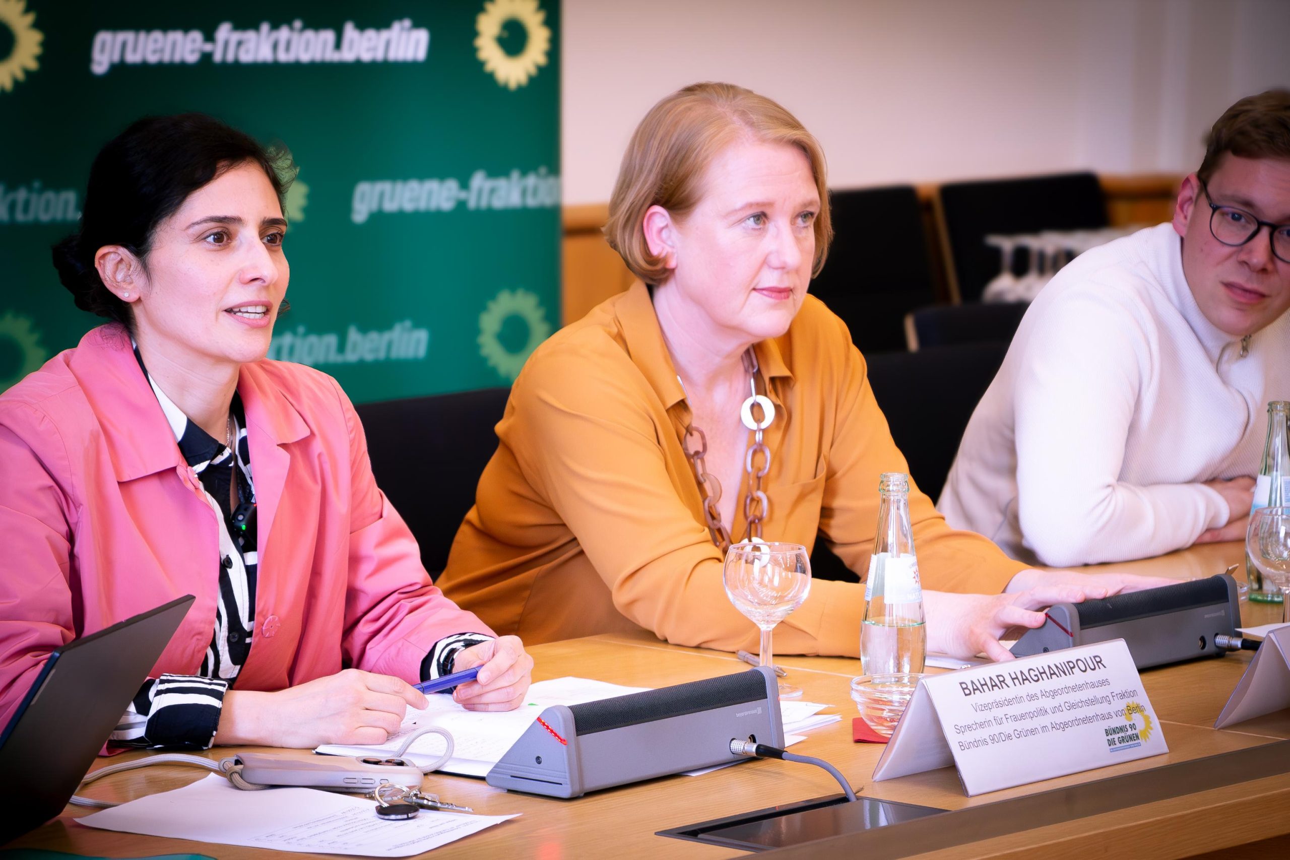 Auf dem Foto sieht man von links nach rechts: Bahar Haghanipour, Lisa Paus und Vasili Franco. Sie sitzen an einem Tisch. Vor ihnen Namensschilder, hinter ihnen Banner der Grünen Fraktion Berlin in dunkelgrün.